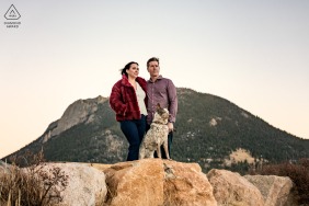 Against a glowing mountain sunset in Rocky Mountain National Park, Colorado, the couple and their dog pose together, the golden light casting a warm glow on their faces and capturing the happiness of their outdoor adventure.
