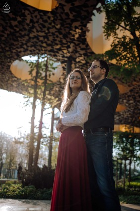 Beneath colorful autumn trees in Budapest, a smiling couple embraces and laughs together along a sunlit path, the golden leaves overhead amplifying the joy and lighthearted energy of their day outdoors.