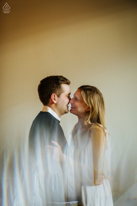 In the Catskills, NY, a couple is about to kiss, their engagement portrait set against the reflective light flairs that highlight the beauty of the surrounding landscape and their connection.
