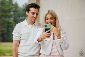 In Hyde Park, NY, a couple shares an intimate engagement portrait, standing together amidst the serene landscape, their connection highlighted by the selfie they are taking with her ring.