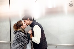Kissing with a telephone box in the background in Grenoble, France, the couple shares a tender moment in the city, their affection delivered within the lively urban setting of this French venue.