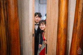 Playfully peeking from behind wooden doors at Chuanmentz Restaurant, Taoyuan, Taiwan, the couple shares a private session of laughter, their joyful excitement echoed by the inviting atmosphere of this unique wedding venue.