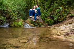 Sitting together on a large boulder beside a small waterfall and clear pool along Sendero del Río Cerezuelo in Cazorla, Jaén, Spain, the couple shares a peaceful engagement portrait surrounded by tranquil nature.