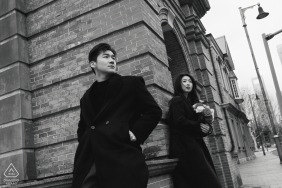 A black-and-white portrait of a couple in Shanghai, leaning against the Bund’s historic brick wall, their engagement portrait reflecting quiet confidence amid the city’s timeless architecture.