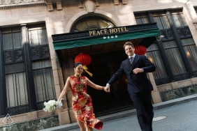 Hand in hand, a couple runs under the shadows of the Peace Hotel in Shanghai, their engagement portrait capturing the blend of tradition and city life in the background.