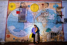 A couple embraces beside a vibrant city wall featuring a colorful painted map at Iron Hill Brewery in Philadelphia, their engagement portrait framed by bold artwork and lively urban textures.