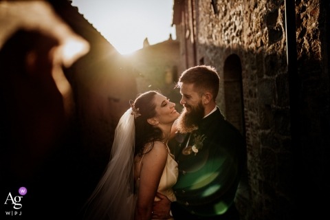 Castello di Gargonza wedding day portrait of a couple  as they smile in the framing inside the small street with a sun flare