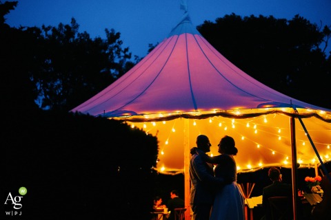 Artistic Cape Cod wedding picture in Falmouth, Massachusetts from a private residence showing the MA couple in front of the tent at dusk with lights