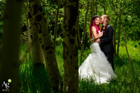 A bride and groom in Colorado share a tender embrace while surrounded by the natural beauty of an Aspen forest, during an off-centered framed portrait session before their wedding ceremony near the location.