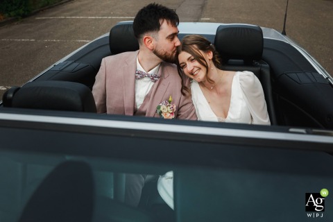 Newlyweds Sit Together in a Convertible Exchanging a Kiss With Radiant Smiles at Church in Metz, France In front of the church, the newlyweds sit together in a convertible, exchanging a tender kiss. Their happiness is displayed through radiant smiles and effortless closeness.