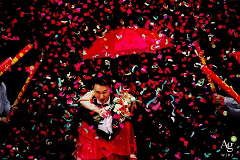 In the groom’s family home in Nanning, Guangxi, he lifts the bride while vibrant red confetti fills the air, bringing a festive and playful scene to their wedding celebration.