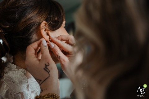 Inside a home in Saumur, France, the bride’s maid delicately helps her with earrings, focusing on those thoughtful final touches that mark the end of bridal preparations.