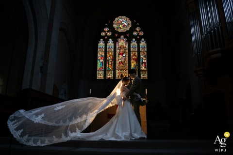 Softly illuminated bride and groom in a Florence, Tuscany church, with a stunning stained glass window behind them.