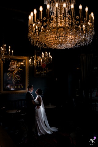 Bride and groom pose under a large, illuminated chandelier in an elegant Kansas City bar.