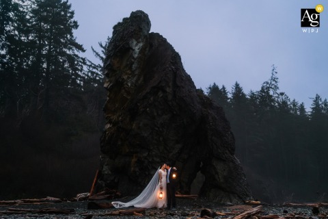 Bride and groom kiss holding lanterns on Olympic National Park beach after adventurous wedding day.