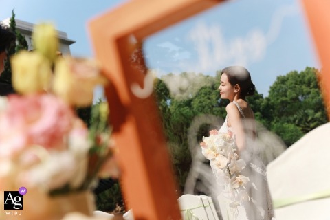 Bride framed by wooden structure, surrounded by blooming flowers and greenery at Millennium Hong Qiao Hotel.