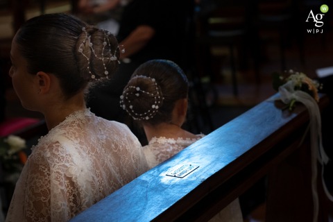 ramatic light catches the intricate hairstyles of the bridesmaids and the textured wooden pews inside the Basilica Minore di S. Benedetto Abate in Mantua, Italy, during the ceremony.