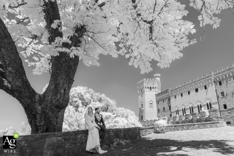 Couple Rests Under Ancient Oak In Dreamlike Portrait At Castello Di Valenzano, Italy The couple rests beneath an ancient oak tree at Castello di Valenzano, Italy, in an infrared portrait that transforms the landscape into a dreamlike and ethereal scene.