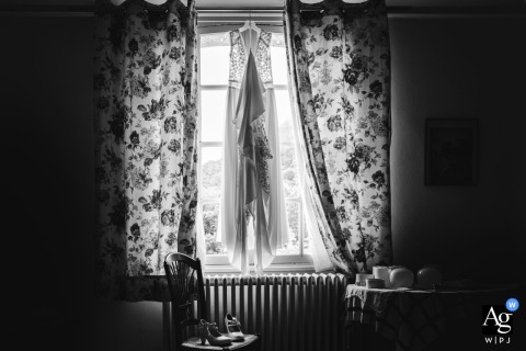 Bride’s dress and shoes hang by window in family home, awaiting her special day in France.