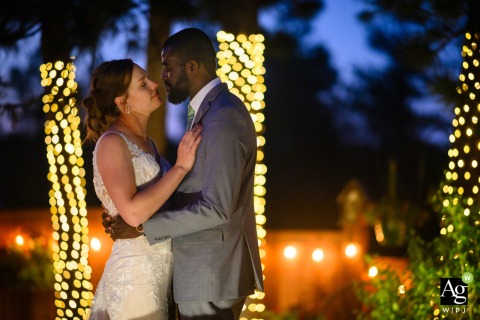 A couple shares a quiet embrace in the soft glow of evening lights at Christies of Genesee, Colorado, as the sky transitions into a deep dusk.