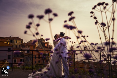 Softly focused foliage silhouettes the foreground as a couple kisses in the background, titled "Flowers of Love" in Tellaro San Michele.