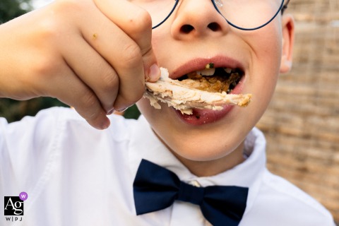 Little boy enjoys eating a chicken wing during cocktail hour at familial pond reception, Villard-les-Dombes.