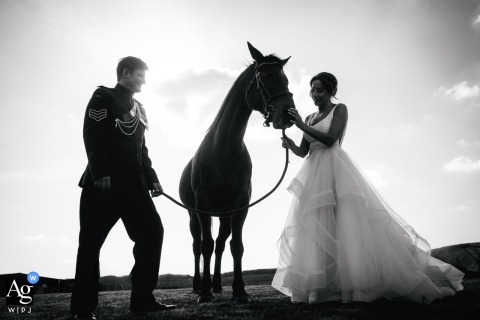 Artistic Black and White Wedding Portrait: Bride, Groom, and Horse at Her Dorset Home An artistic black and white wedding portrait of the bride and groom at her Dorset, England home, standing thoughtfully with their horse.