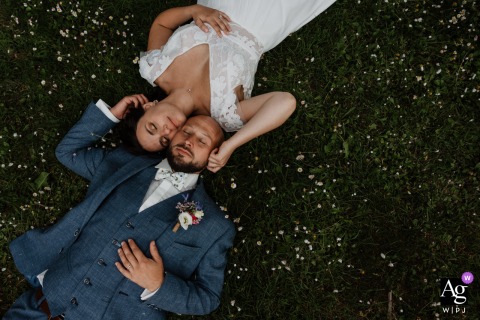 Bride and groom lying in the grass among daisies, eyes closed and relaxed, during their couple's session at Le Fief des Cordeliers, Montjean sur Loire, France.