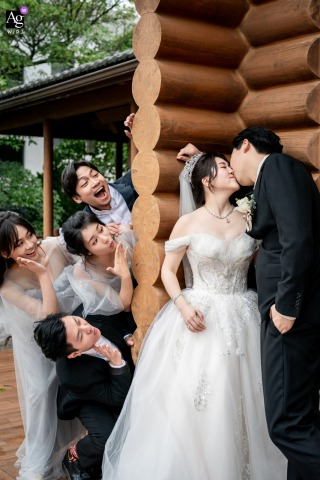 Wooden, Miaoli, Taiwan: Bridesmaids and groomsmen secretly watch a kissing couple outside a log cabin.