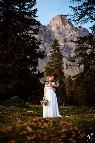 Tall vertical shot of the bride and groom hugging in front of majestic mountains, tall trees, and rock formations at their Solalex, Switzerland reception venue.