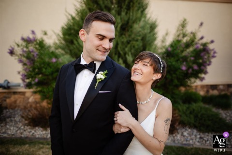Bride and groom beaming at each other during wedding portraits at The Pinery at The Hill, Colorado Springs, CO, with her holding his arm from behind.
