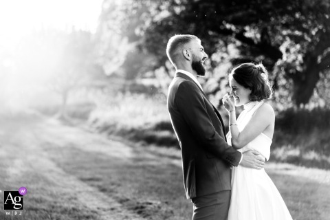 A fun, relaxed black and white golden hour portrait of a happy couple at Talton Lodge, Warwickshire, with a burst of sunlight from behind on the left.