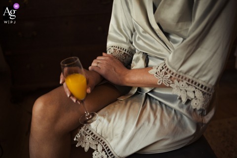 The bride at Chateau Lartigolle, Auch, France, holds a glass of orange juice, set against a black background with soft lighting.