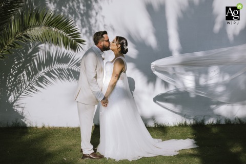 A romantic couple shares a kiss at Three Palms İzmir as the bride's long veil flies dramatically in the wind against the beautiful backdrop of the Turkish coast.