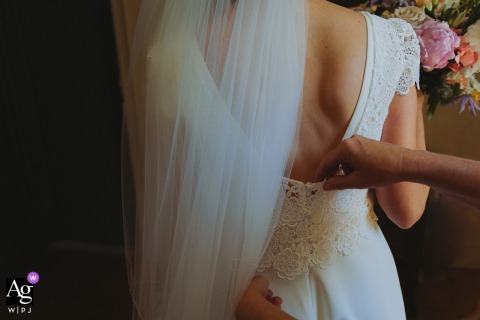 Detail shot of a wedding dress at Chateau de Malliac, Condom, France, with hands seen helping to adjust it.