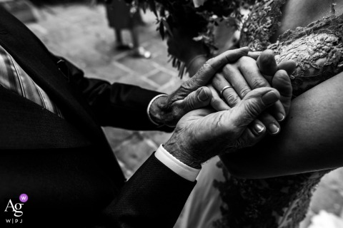 A black and white detail shot with soft side lighting, capturing a tender, emotional moment as a grandfather tightly holds the new bride's hands at Harrogate Registry Office, England.