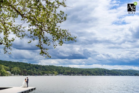 Standing on a wooden dock at Lake Mohawk Country Club in Sparta, New Jersey, the bride and groom pose together under a vast sky filled with beautiful, dramatic clouds.