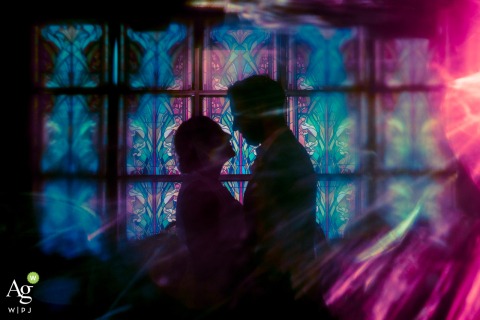 A silhouette of a couple is cast against colorful stained glass at The Loft at Lena’s in Alexandria, Virginia, accented by a soft and artistic lens flare.
