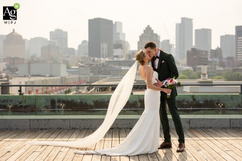 The wedding couple shares a romantic kiss on the roof of the Montreal Science Centre at sunset, with the Quebec city skyline providing a dramatic and urban backdrop.