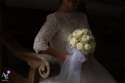 A close-up artistic portrait in Guastalla, Reggio Emilia, Italia, captures the bride's exquisite wedding bouquet and the delicate lace detail of her bodice as she sits in perfect light before leaving.