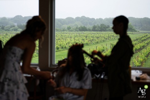 A bridesmaid is silhouetted against the scenic vineyard landscape of Saltwater Farm Vineyard in Stonington, Connecticut, as she has her hair styled before the wedding ceremony begins. 