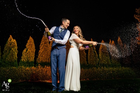 At Chestnut Ridge in Canton, North Carolina, a gelled light illuminates the background shrubs to create depth and vibrant color during an energetic champagne spray celebration with the couple.