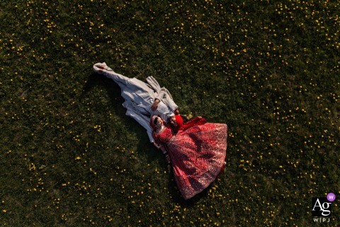 Winnipeg: After their wedding ceremony, a drone photo captures a serene, artistic portrait of the newlyweds laying down amidst a vibrant field of yellow dandelion flowers.