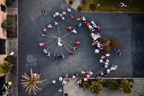 Hauts-de-France, Nord - An artistic overhead drone view captures the reception venue where wedding guests are engaged in a dynamic ribbon game, creating a striking scene setter on the couple's special day.