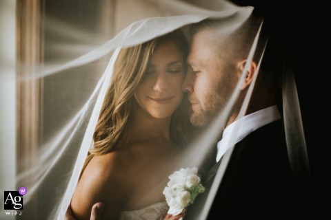 A lovely, intimate portrait taken in Bratenahl, OH, shows the bride smiling warmly while embracing the groom by a window, utilizing the soft available indoor light.