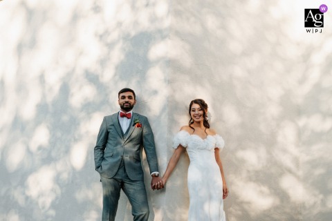 Whitehouse Station, NJ, provides the backdrop for a portrait of a couple holding hands against a stucco wall, illuminated by splattered, dappled sunlight from overhead trees.