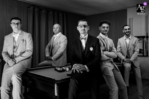 In Paladru, Isère, France, a black-and-white portrait at the groom's house captures the groom and his best men seated and standing casually around a billiard table.