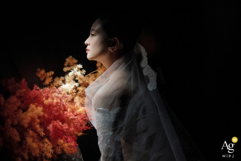 At LongBai 18, Shanghai, China, a minimalistic portrait features the bride standing in profile beside an autumn-hued floral arrangement, dramatically illuminated by bold, artistic light.