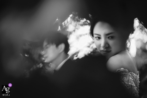 In Shanghai, China, an artistic black-and-white portrait captures the couple partially obscured and diffused through the gaps in a dense curtain of leaves.
