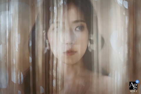 In Shanghai, China, an artistic portrait captures the bride obscured by a curtain of light-colored, shimmering strands, creating a diffused and ethereal effect.